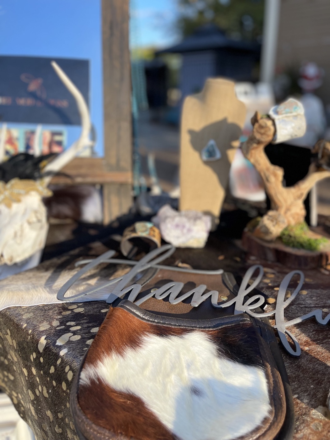 An outdoor pop-up booth with antlers, a thankful sign, a jewelry stand and a cowhide bag