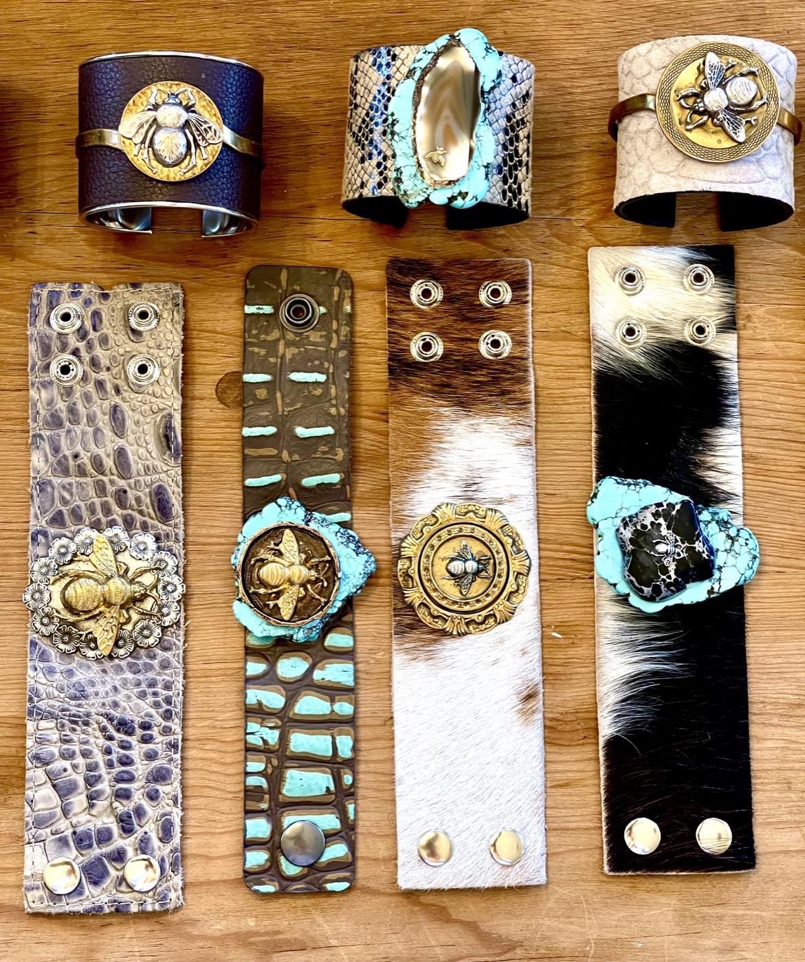 Leather cuffs with bee medallions and turquoise stones laid flat on wood