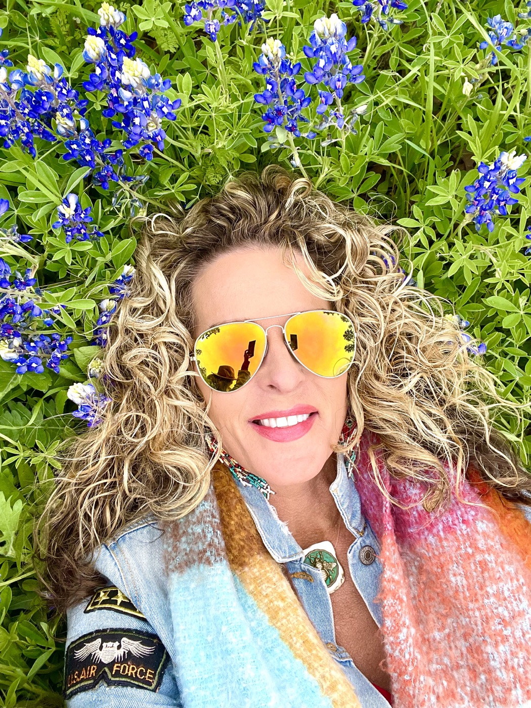 Stephanie lying in a field of bluebonnets in mirrored aviators and a colorful scarf